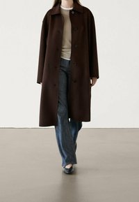 Brauner Wollmantel mit lockerer Passform, großem Kragen und Knopfverschluss, kombiniert mit einem hellen Oberteil und weiten Denim-Jeans.