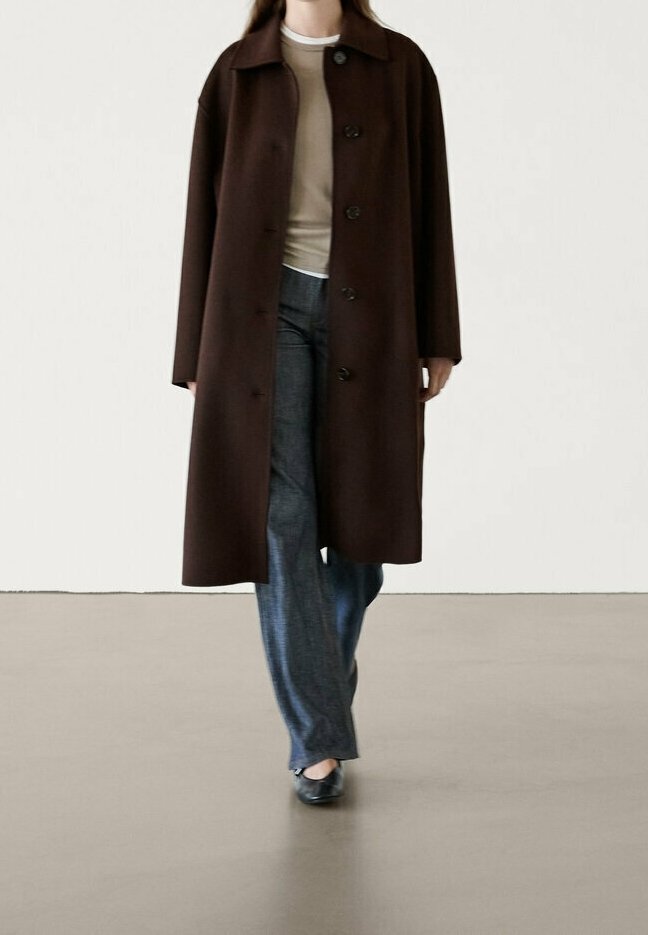 Brauner Wollmantel mit lockerer Passform, großem Kragen und Knopfverschluss, kombiniert mit einem hellen Oberteil und weiten Denim-Jeans.