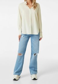 Kremowa koszula z guzikami, wykonana z teksturowanej tkaniny, w zestawieniu z jasnoniebieskimi dżinsami z przetarciami i dziurami.