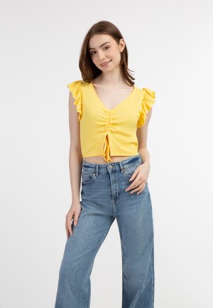 Gul ribbet crop top med flæser på ærmerne og en frontsløjfe, parret med højtaljede lyseblå vide jeans.