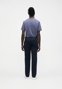 Camiseta azul marino de manga corta combinada con pantalones oscuros; costuras visibles, tela texturizada y zapatillas blancas sobre un fondo liso.