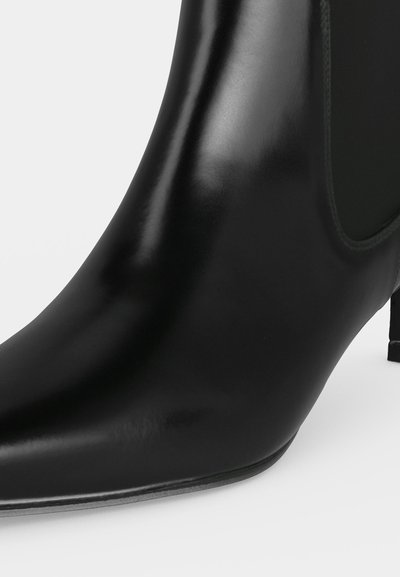 Gros plan sur une bottine noire en cuir, à bout arrondi, avec un empiècement latéral cousu et un talon bas.