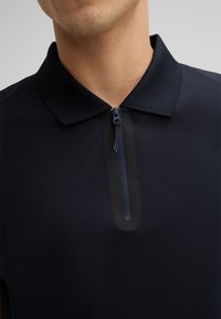 Granatowa koszulka polo z teksturowanej tkaniny, z przodem na pół zamku i jednolitą kołnierzykiem. Minimalistyczny design i subtelne akcenty.