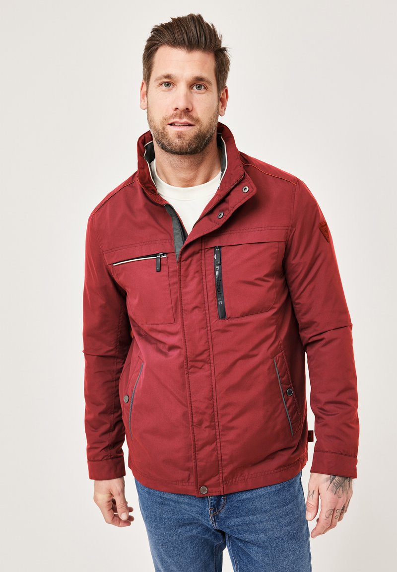 Red insulated jacket with a high collar, zippered chest pocket, side pockets, and gray accents. Features a water-resistant material.
