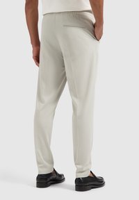 Light gray trousers made of a smooth fabric with an elastic waistband, featuring a back pocket and tapered leg design.