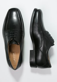 Zapatos de vestir de cuero negro con una textura suave, punta redonda, diseño con cordones y sutiles detalles de costura. Suelas de goma para mayor tracción.