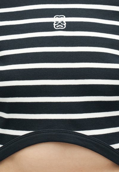 Υφασμα με οριζόντιες ριγέ σε ασπρόμαυρο, με ένα μικρό κεντητό λευκό λογότυπο θυμωμένου προσώπου στο κέντρο κοντά στην κορυφή.