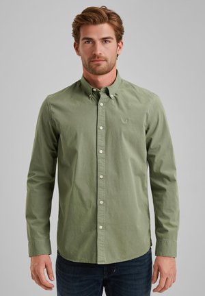 Green cotton button-up shirt with a pointed collar and white buttons. Features subtle logo embroidery on the chest. Worn with dark jeans.