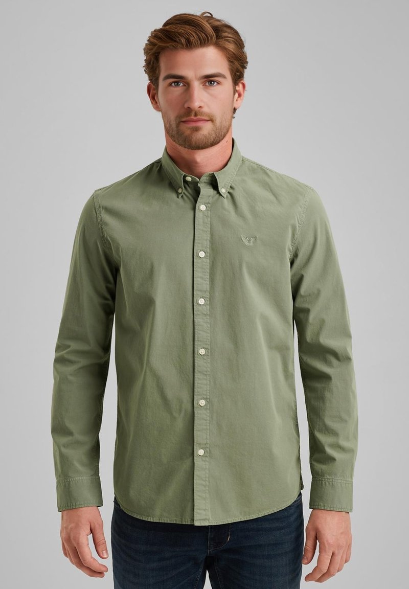 Camicia button-up verde in cotone con colletto a punta e bottoni bianchi. Presenta un ricamo del logo in modo sottile sul petto. Indossata con jeans scuri.