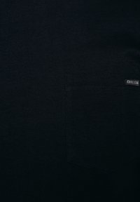 Czarny materiał z naszytą prostokątną kieszenią po prawej stronie, z małą metką marki "Big Star" w górnym rogu.