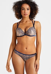 Soutien-gorge en dentelle et bikini assorti en nude avec des accents marine ; comporte des motifs floraux complexes, des bretelles ajustables et une texture douce.