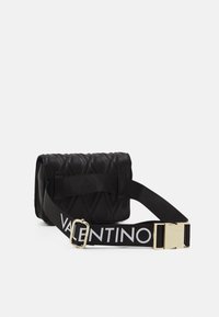 Borsa nera trapuntata con superficie textured e una tracolla larga decorata con logo. Presenta un accento di fibbia dorata. Forma rettangolare compatta.