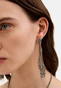 Pendientes de plata con una base de perno redondo y largas cadenas en cascada adornadas con pequeñas cuentas metálicas, creando un aspecto texturizado y en capas.