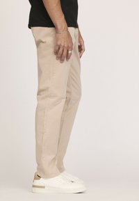 Chinos beiges en coton, avec une coupe près du corps, des poches latérales et une texture lisse, associés à des baskets blanches avec un accent marron clair.
