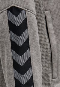 Grauer Pullover mit einer strukturierten Stoffoberfläche und einem schwarzen Einsatz, der weiße gestreifte Chevron-Muster an der Seite zeigt.