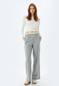 Lichtgrijze, gestreepte, wijde broek met een elastische tailleband, trekkoorddetail, twee zijzakken, gecombineerd met een aansluitend shirt met lange mouwen.