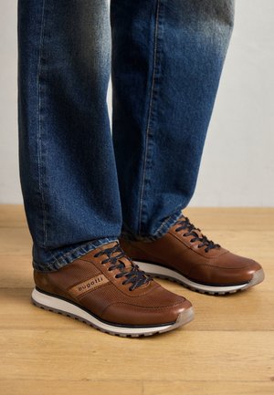 Pruun nahast spordijalatsid tekstureeritud külgpaneelidega, valge kummist tald, mustad paelad ja "bugatti" logo küljes, kantud koos siniste teksadega.