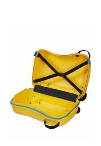 Valise rigide jaune ouverte, montrant des sangles croisées noires, une fermeture éclair bleue, une poignée et des compartiments intérieurs arrondis sur fond blanc.