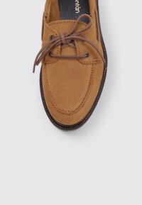 Braune Wildleder-Bootsschuh mit abgerundeter Zehe, Schnürdesign und kontrastierender, strukturierter brauner Gummisohle. Zugnäht sind sichtbar auf dem Obermaterial.