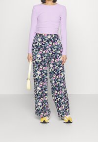 Lila långärmad figurnära topp i kombination med marinblå blommiga vida byxor. Byxorna har en blandning av färgglada blommor, med en mjuk textur och lätt design.