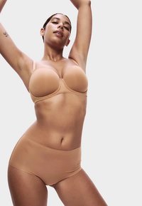Béžová sada podprsenky a kalhotek s vysokým pasem z hladké tkaniny. Podprsenka má tvarované košíčky a nastavitelné ramínka. Jednoduchý, bezešvý design.