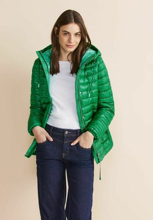 Groene gewatteerde pufferjas met capuchon, ritsopening en trekkoorddetails. Gecombineerd met donkerdenim jeans en een witte top. Glad, glanzend materiaal.