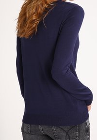 Pull en tricot bleu marine à manches longues, avec un ourlet ajusté et une texture lisse. Design minimaliste, sans motifs ni accents visibles.