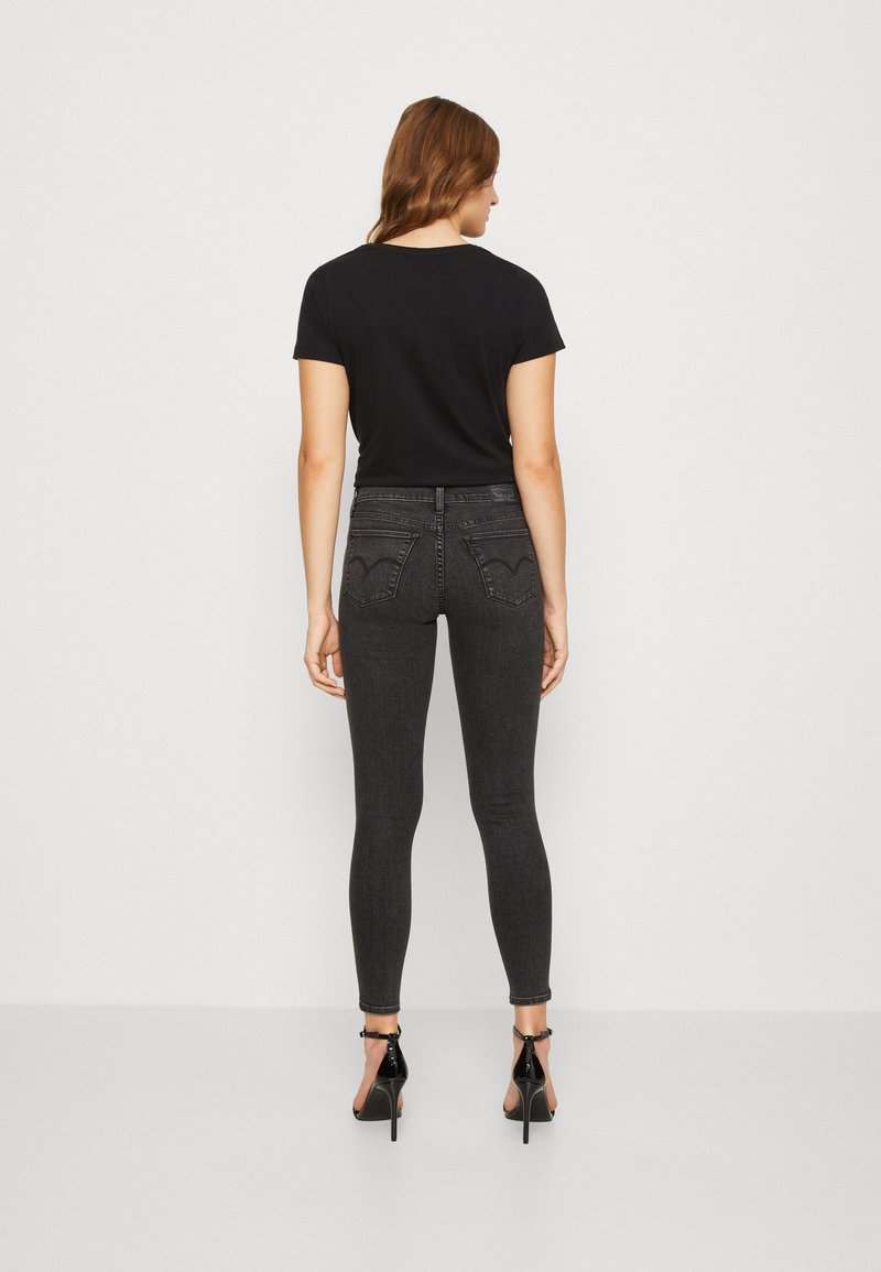 Camiseta negra ajustada, jeans oscuros de talle alto y tacones negros con tiras al tobillo. Los jeans tienen bolsillos traseros con detalles de costura.