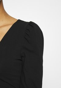 Schwarze Bluse mit tiefem V-Ausschnitt und Puffärmeln. Der Stoff ist glatt mit einem leichten Stretch und betont eine figurbetonte Silhouette.