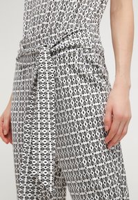 Tutina a righe bianche e nere con vita arricciata e dettagli di cintura annodata. Presenta un mix di design geometrici e ispirati agli animali.