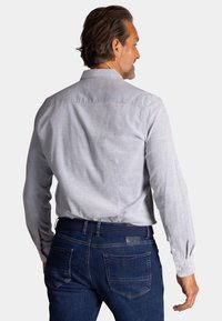 Lichtgrijs overhemd met lange mouwen, een kraag, knoopmanchetten en een gestructureerde stof, gecombineerd met donkerblauwe jeans met zichtbare achterzakken.