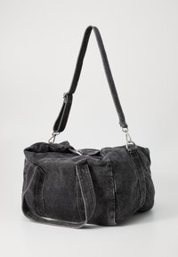 Mala de duffel em denim preto com alças duplas e correia de ombro ajustável. Textura macia, fecho com zíper e detalhes de costura branca visíveis.