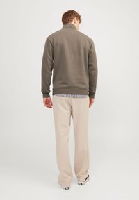Grijze sweatshirt met een hoge kraag, van achteren getoond, gecombineerd met lichtbeige trousers en zwarte sneakers. Soepele stoftextuur.