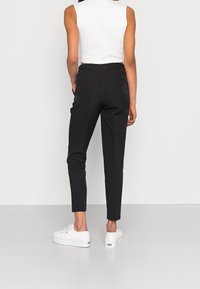 Pantalon noir fuselé avec une texture lisse, dotée de poches arrière et d'une taille haute. Associé à des baskets blanches et un haut blanc côtelé.