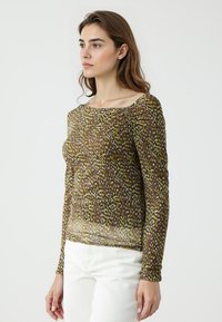 Blouse marron à manches longues avec un design à motifs en jaune et blanc, présentant un col bateau et une texture légère et transparente.