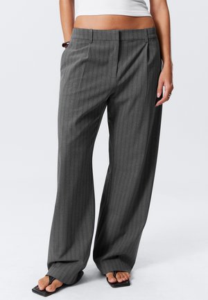 Woman wearing high-waisted, wide-leg gray pinstripe trousers with black square-toe sandals and a white crop top, standing against a plain background.