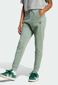 Gröna sweats med en avsmalnande design, som har en sidoficka och en broderad logga. I kombination med gröna sneakers och vita strumpor.