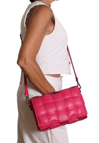 Borsa a mano in pelle rosa con un design imbottito, dotata di una tracolla removibile e una forma rettangolare strutturata.