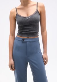 Szary prążkowany top na ramiączkach z koronkowym wykończeniem, z małą kokardką na środku. W połączeniu z jasnoniebieskimi, dopasowanymi spodniami z guzikiem z przodu.