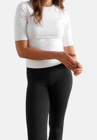 Top bianco aderente con maniche corte, texture liscia e scollatura rotonda. Abbinato a leggings neri, in tessuto elastico e design aderente.