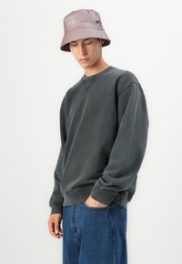 Sudadera de algodón gris con cuello redondo, combinada con un sombrero tipo cubo en rosa claro. El modelo lleva puestos unos vaqueros de denim azul de corte relajado.