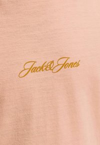 Tissu rose clair avec le logo "Jack & Jones" en écriture cursive dorée imprimé au centre.