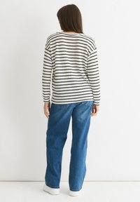 Knitted sweater with black and white horizontal stripes, paired with blue denim jeans and white sneakers. Simple, relaxed fit design.