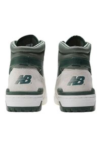Zapatillas altas con un acabado superior de ante gris y acentos verdes, cuello acolchado y suela de goma blanca. Logo de New Balance en el talón.