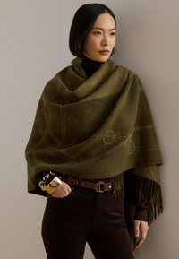 Șal verde măsliniu cu margini franjurate, având un design subtil în model; asortat cu o centură maro și pantaloni închiși la culoare.