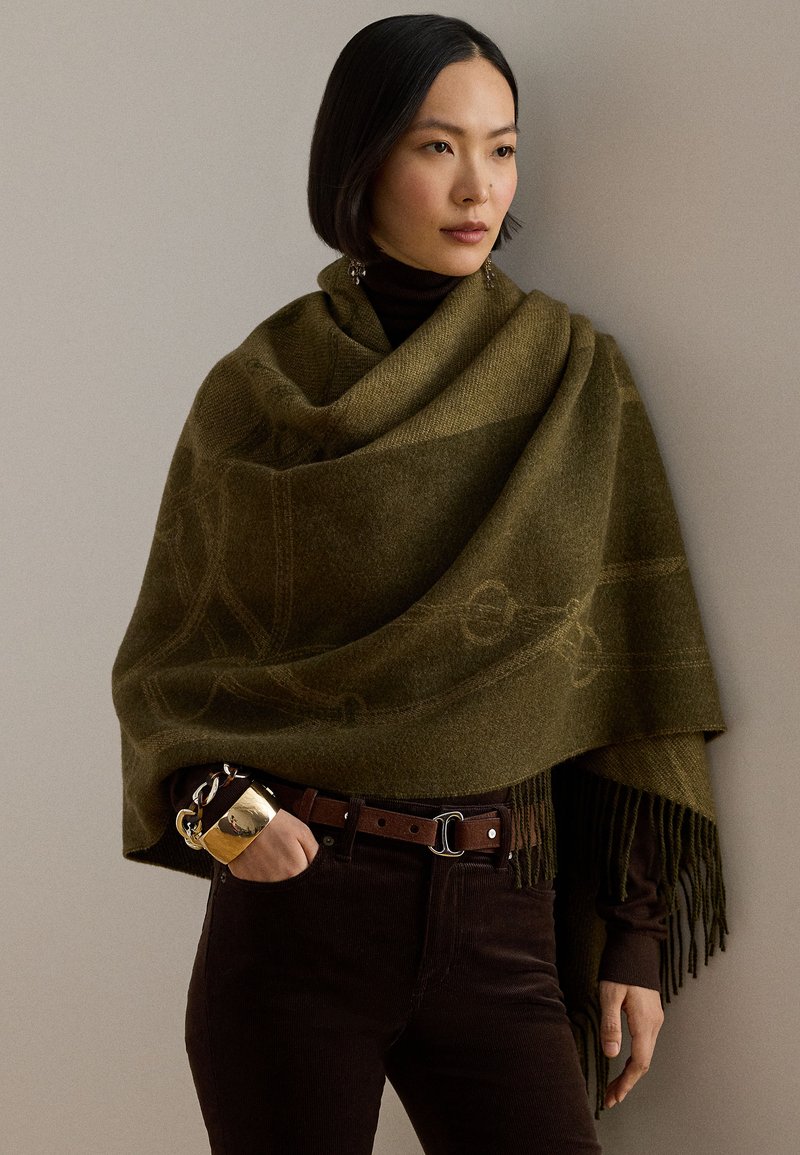 Șal verde măsliniu cu margini franjurate, având un design subtil în model; asortat cu o centură maro și pantaloni închiși la culoare.