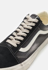 Baskets noires et grises avec une tige lisse et texturée, une bande d'accent blanche, des lacets beiges et une semelle en caoutchouc avec une bande de roulement à motif.