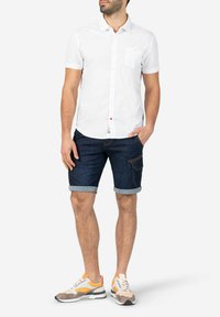 White short-sleeved button-up shirt, dark denim shorts with rolled cuffs, and color-blocked sneakers featuring orange and gray accents.