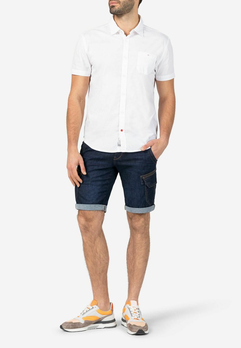 White short-sleeved button-up shirt, dark denim shorts with rolled cuffs, and color-blocked sneakers featuring orange and gray accents.
