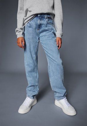 Jean bleu clair, ample, en denim, avec un design classique à cinq poches. Associé à des baskets blanches et un pull gris.